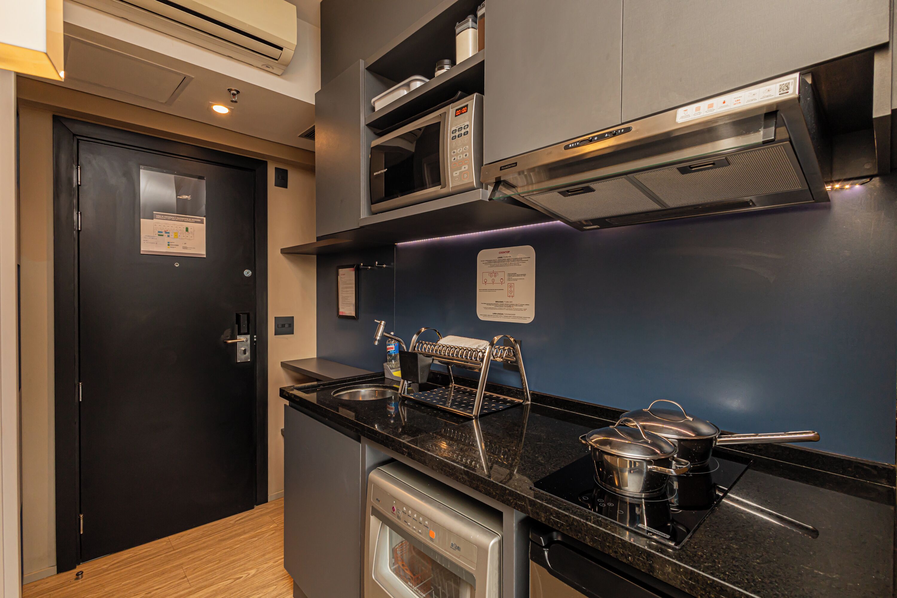 A compact kitchen with a black countertop, stainless steel appliances, and a microwave above the stove.