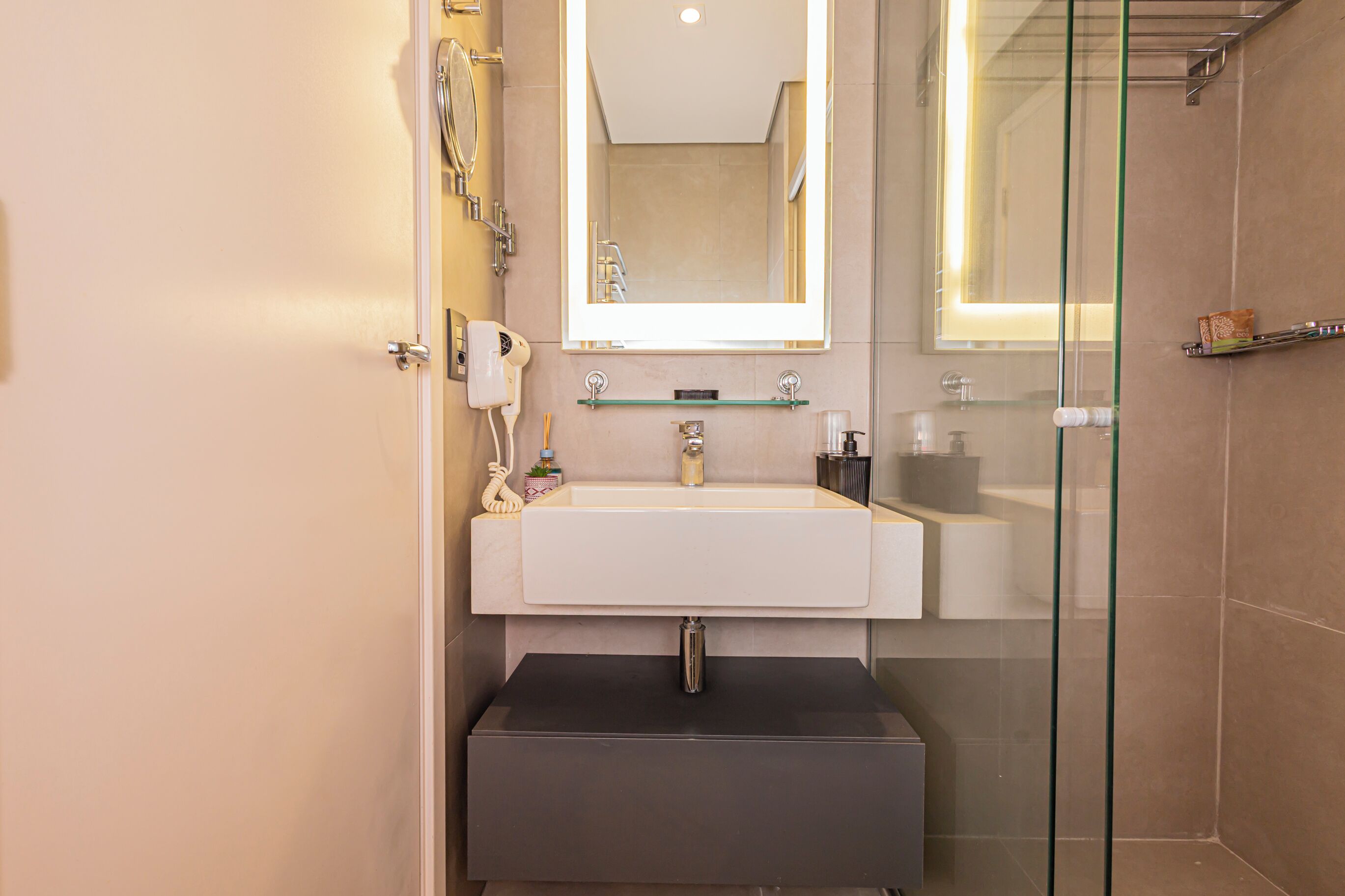 Un baño moderno con un espejo grande, un lavamanos y una zona de ducha con mampara de vidrio.