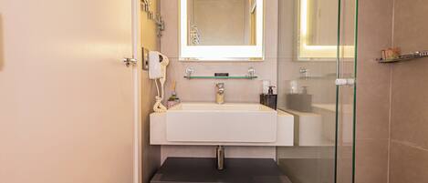 Un baño moderno con un espejo grande, un lavamanos y una zona de ducha con mampara de vidrio.