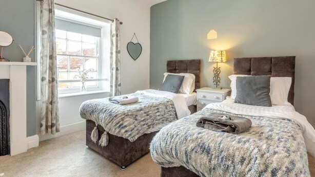 Un dormitorio con dos camas, una ventana con cortinas, una lámpara de noche y una decoración con forma de corazón en la pared.