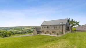 A stone farmhouse with a sloped roof, a small attached structure, and a grassy yard. - 4 Bed in Beguildy (oc-t41741) (Beguildy)