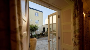 An open door leading to a courtyard with a potted plant, a stone fountain, and a building in the background. - 2 Bed in Oxford (oc-s41047) (Oxford)