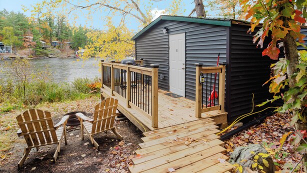 A cabin with a dock, two Adirondack chairs, and a view of a lake.
