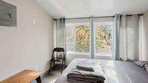 A bedroom with a bed, a chair, a window with curtains, and a wooden bench.