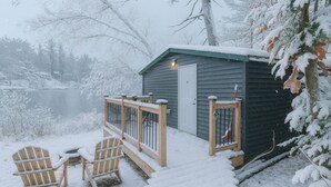 A wooden deck with chairs and a small shed with a door and window.