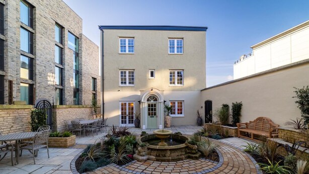 Un patio con una fuente, mobiliario exterior y un edificio con puerta y ventanas.