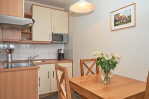 A kitchen with wooden cabinets, a microwave, a coffee maker, a sink, and a dining table with chairs. - Seepark Sellin Fewo fur 3 Personen (Sellin)