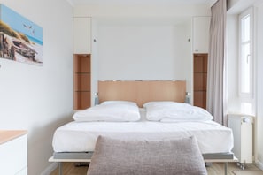 A bedroom with a bed, a bedside table, a chair, a wardrobe, and a window with curtains. - Fantastisches Studio im Seepark Sellin mit Balkon (Sellin)