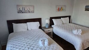 Duas camas de casal com roupa de cama branca, uma mesa de cabeceira com abajur e obras de arte nas paredes.