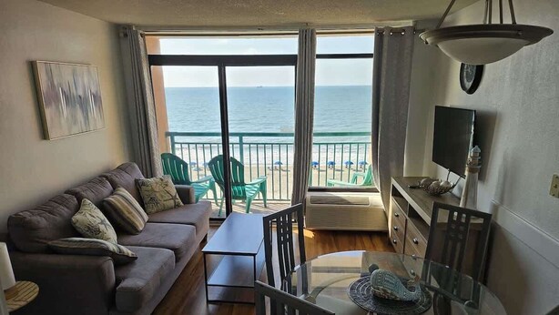 Uma sala de estar com sofá, cadeiras, mesa de vidro e vista para o oceano.