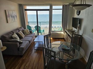 Un salon avec un canapé, des fauteuils, une table en verre et une vue sur l’océan.