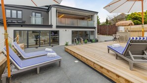 Uma casa moderna de dois andares com um espaço de pátio com espreguiçadeiras e guarda-sóis.