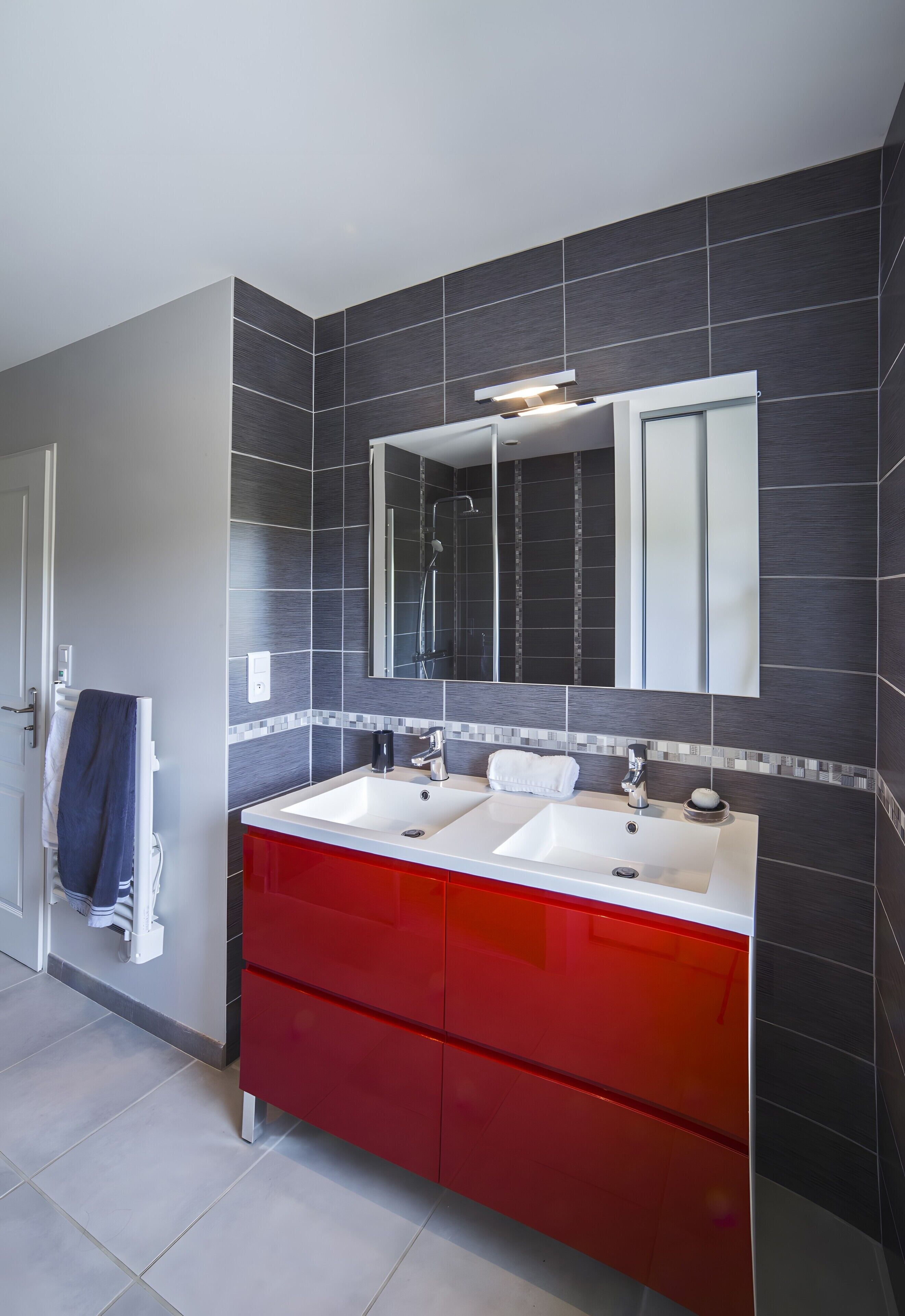 Un bagno con due lavandini, un mobile contenitore rosso e uno specchio grande.