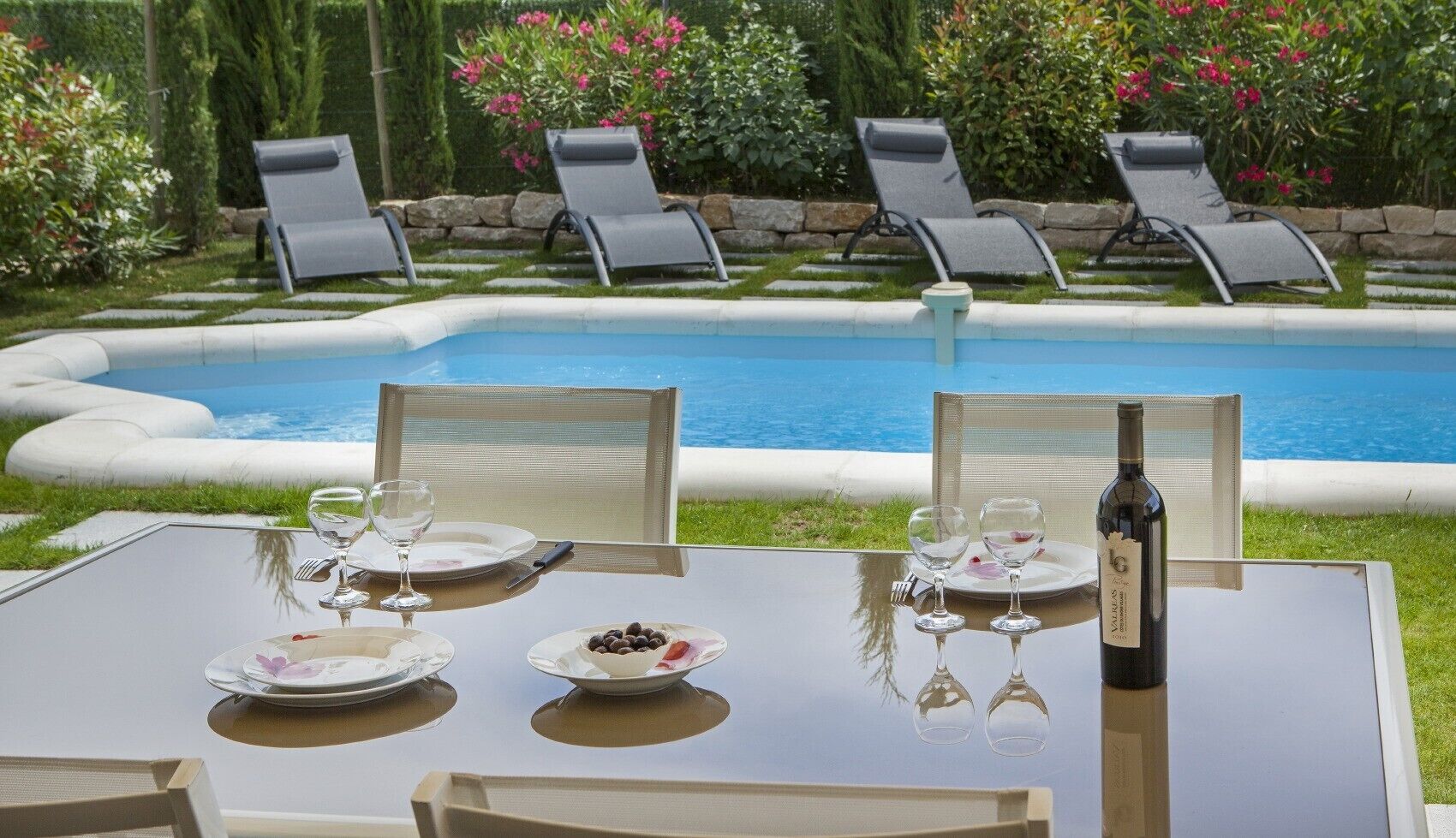 Ein Tisch mit Stühlen am Pool, eine Weinflasche und Teller mit Besteck.