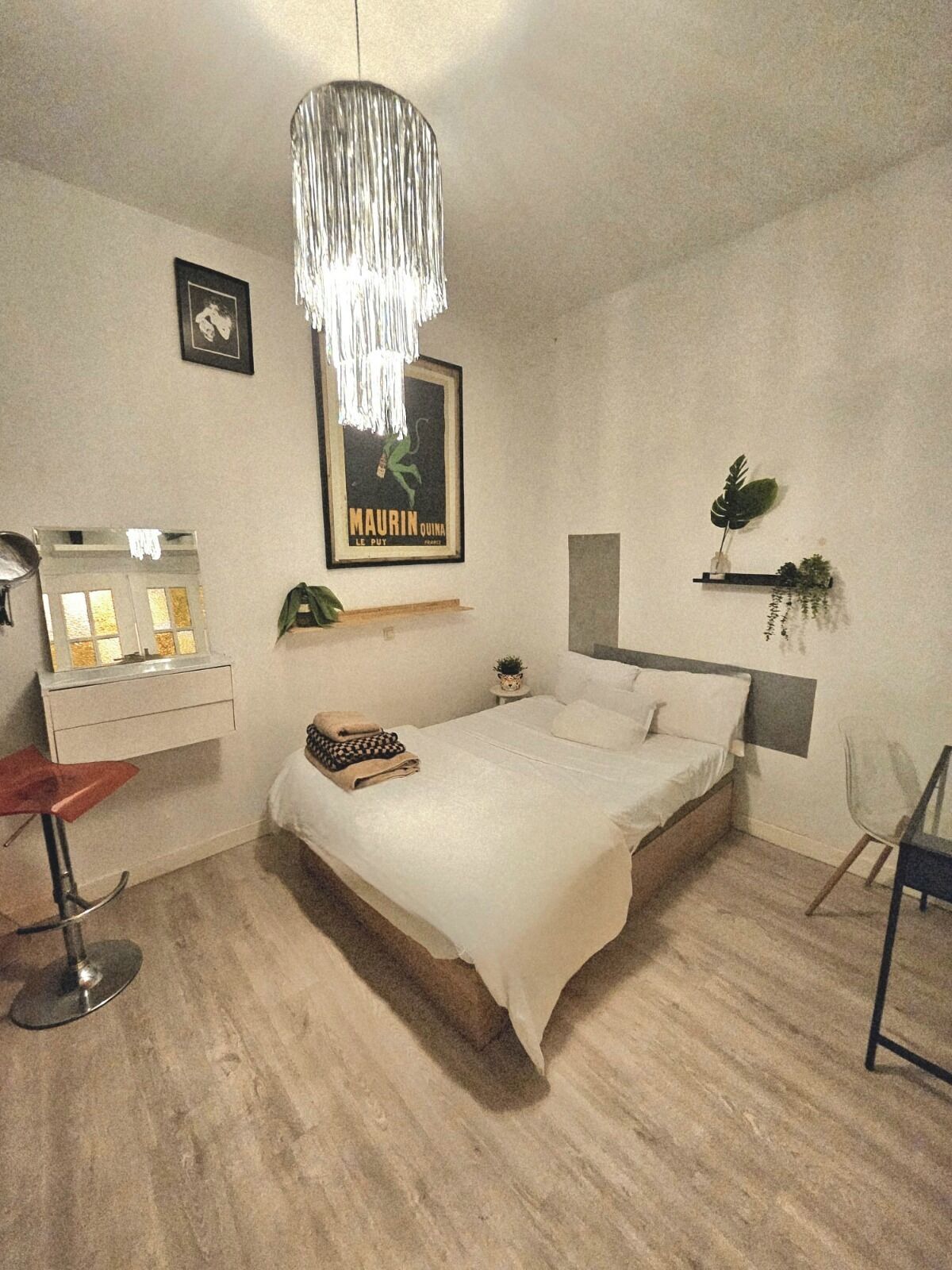 Een slaapkamer met een bed, een hanglamp, een klein plantje en een lijstje met een foto aan de muur.