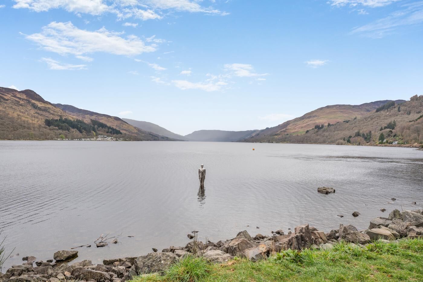 A calm lake with a rocky shoreline and hills in the background.