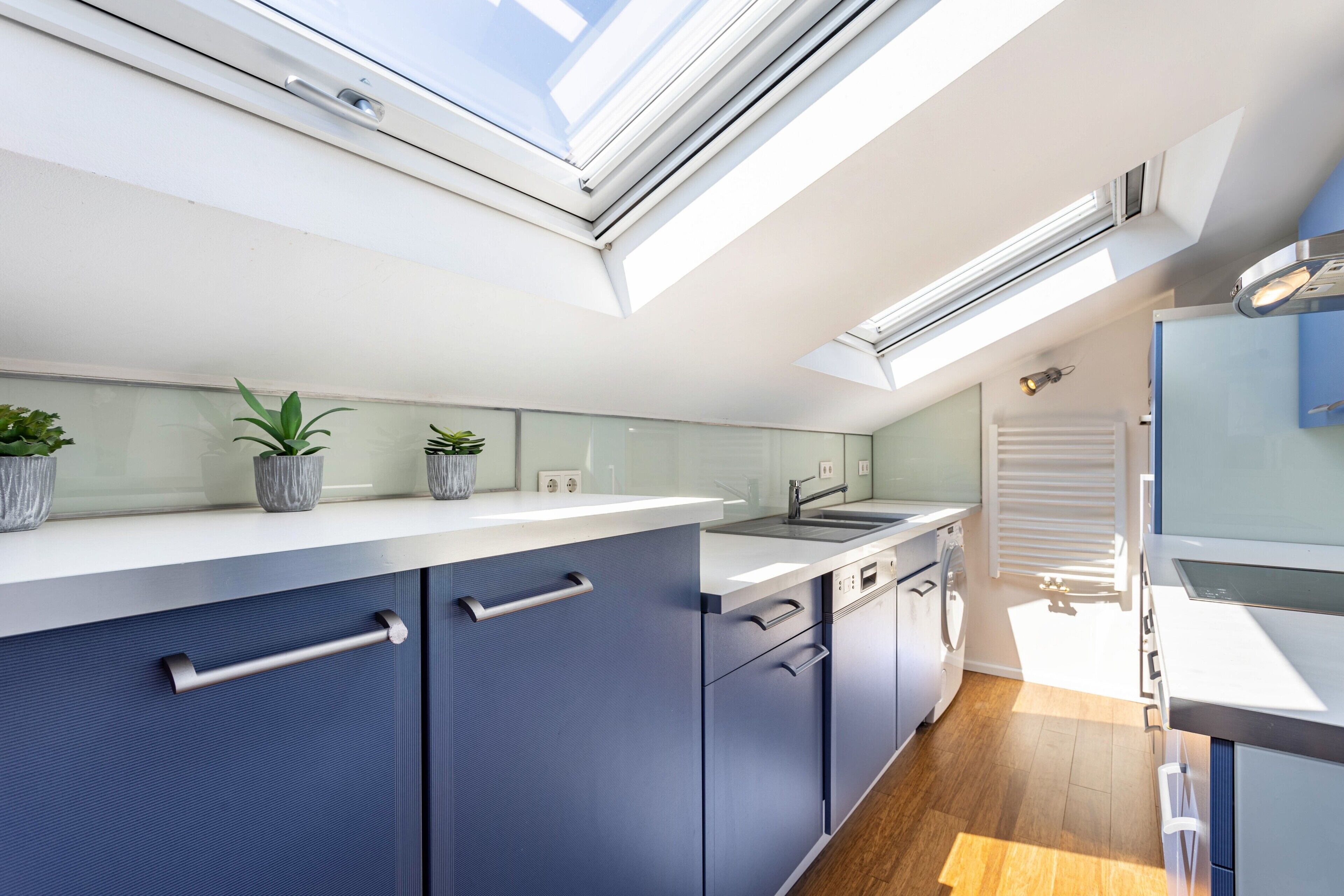 A modern kitchen with skylights, a built-in dishwasher, and a window with blinds.