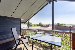 A balcony with a table and chairs, a view of a parking lot, and a building in the background.