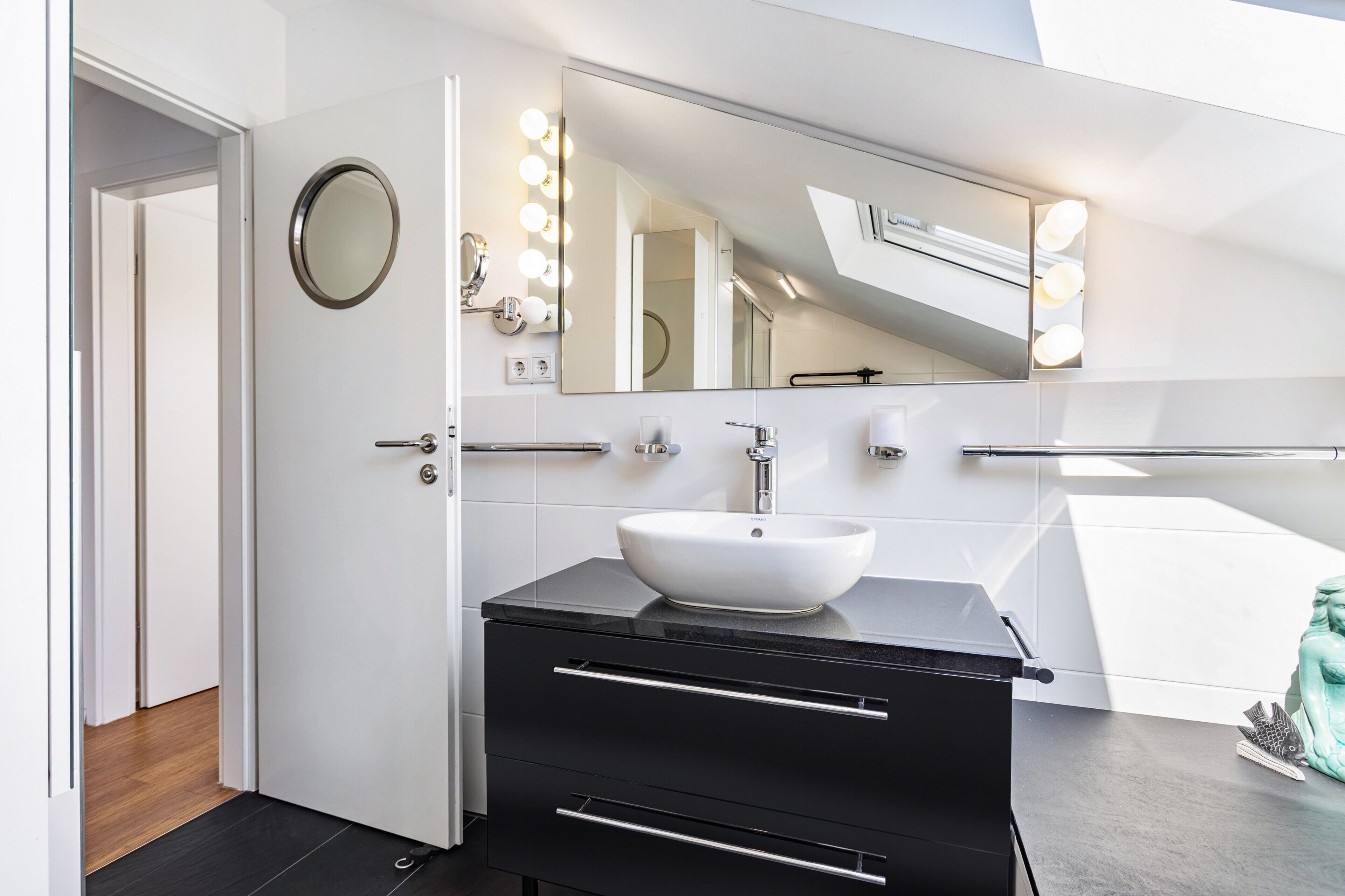 A modern bathroom with a white sink, black vanity, and a large mirror with lights.