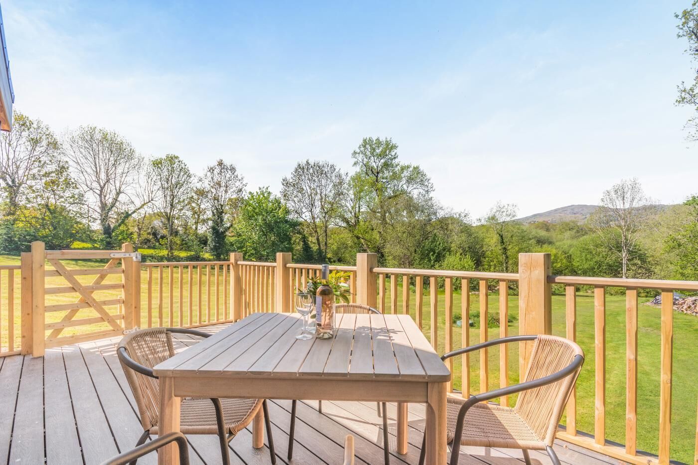 Une terrasse en bois avec une table et des chaises, une bouteille de vin et un verre.
