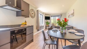 A modern kitchen with a built-in oven and a dining area with a round table and chairs. - 2 Bed in Tyn-y-Groes (oc-w42450) (Ty'n-y-groes)