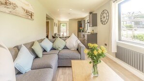 A modern living room with a grey sectional sofa, a wooden coffee table, and a vase of yellow flowers. - 2 Bed in Tyn-y-Groes (oc-w42450) (Ty'n-y-groes)