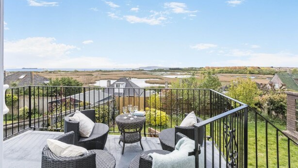 A balcony with wicker furniture, a small table, and a view of a coastal landscape. - 3 Bed in Weymouth (oc-f41734) (Weymouth)