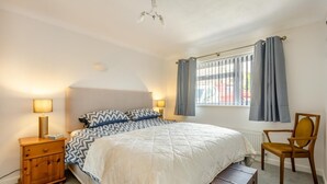 A bedroom with a bed, bedside lamps, a chair, a window with curtains, and a radiator. - 3 Bed in Weymouth (oc-f41734) (Weymouth)