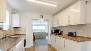 A modern kitchen with white cabinets, a wooden countertop, a sink, a dishwasher, a microwave, and a toaster. - 3 Bed in Weymouth (oc-f41734) (Weymouth)