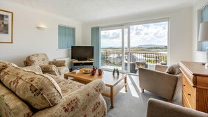 Een woonkamer met een flatscreen televisie, een bank met bloemenprint, een houten salontafel en een balkon met uitzicht.