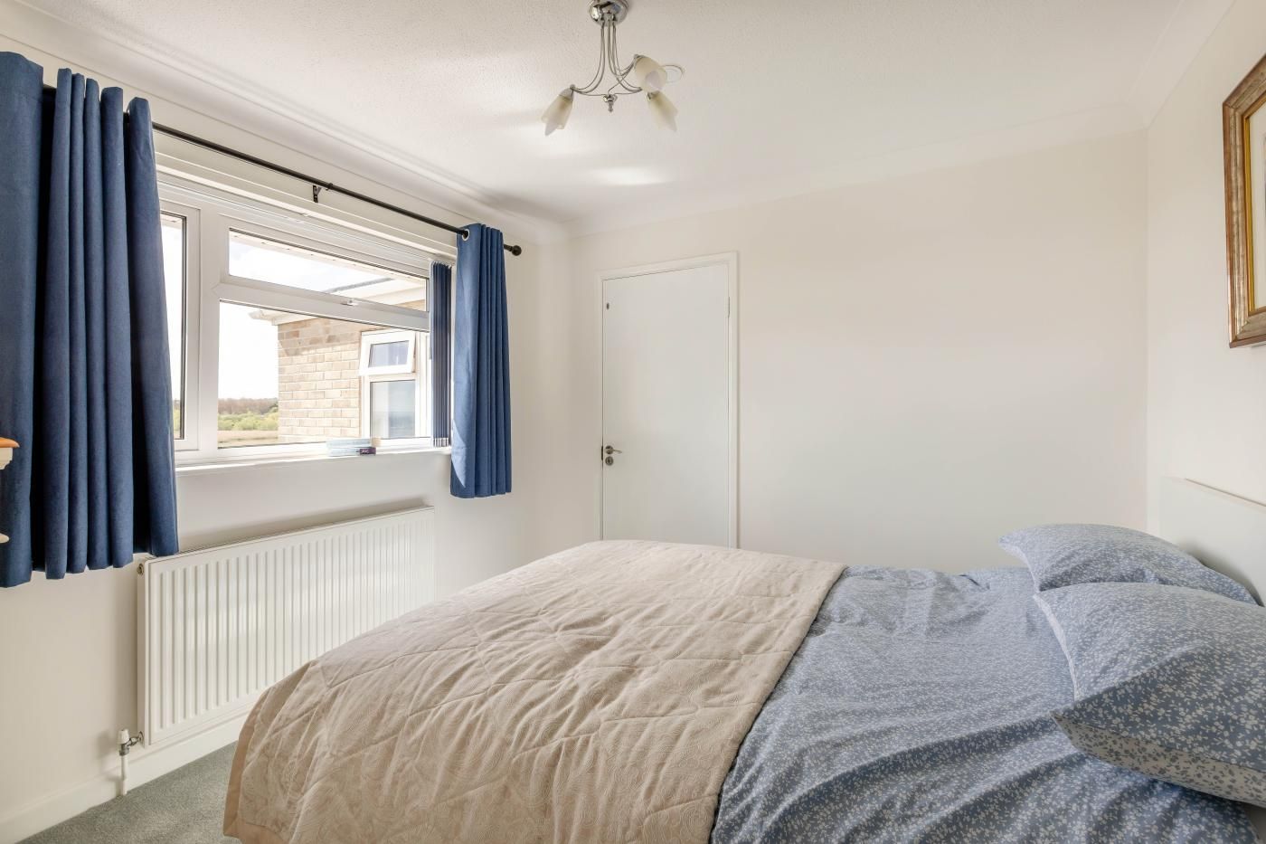 A bedroom with a bed, a window with curtains, a radiator, and a door.