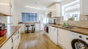 Een moderne keuken met witte kastjes, een houten aanrechtblad, een inbouw vaatwasser en een raam met zonwering.