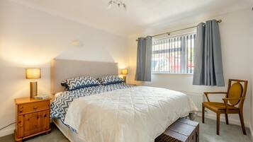 A bedroom with a bed, bedside lamps, a chair, a window with curtains, and a radiator.