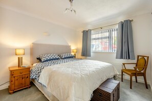 A bedroom with a bed, bedside lamps, a chair, a window with curtains, and a radiator.