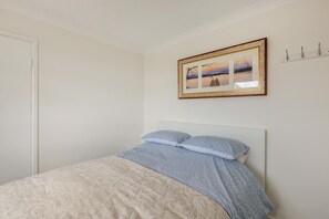 A bedroom with a bed, a framed picture on the wall, and a coat rack.