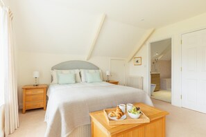Ein Schlafzimmer mit Bett, Nachttischen, einem Tablett mit Croissants und Obst sowie einem durchgegangenen Tür sichtbar erkennbaren Badezimmer.