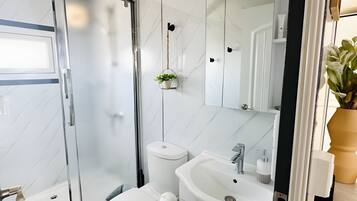 Un baño moderno con cabina de ducha de vidrio, inodoro, lavamanos con espejo y una pequeña planta en maceta.