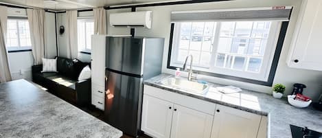 Cocina moderna para vehículo recreativo, con refrigerador de acero inoxidable, un lavamanos y ventana con vistas a edificios.