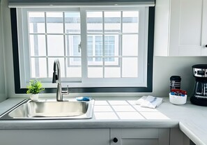Una cocina moderna con un ventanal grande, un lavamanos de acero inoxidable y una cafetera sobre la encimera.