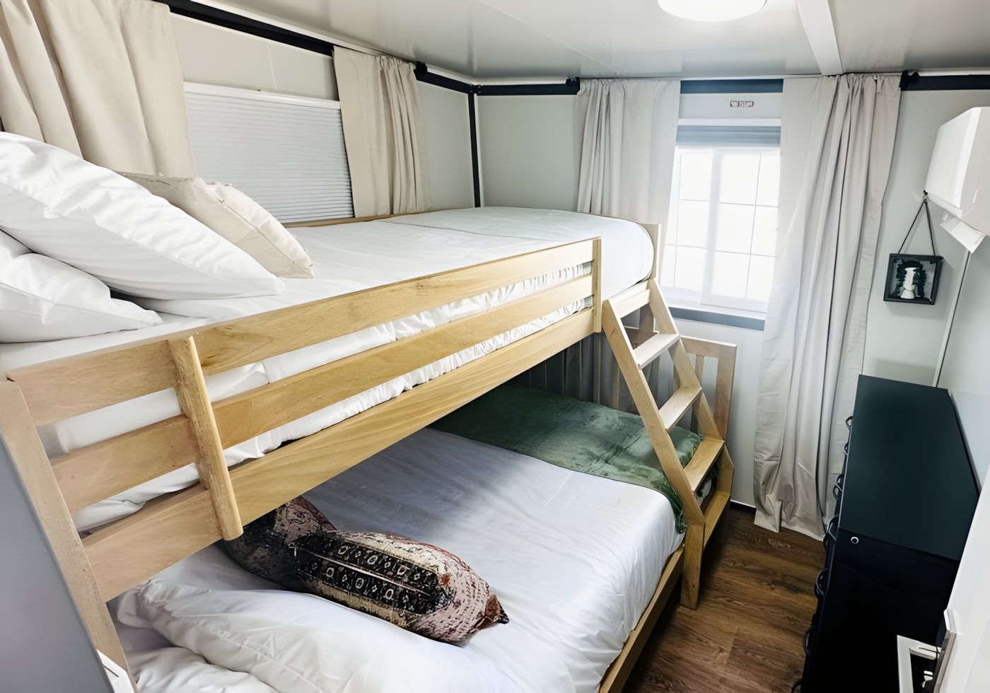 A bunk bed room with a window, curtains, and a desk.