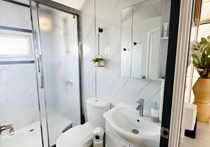 Un baño moderno con cabina de ducha de vidrio, inodoro, lavamanos con espejo y una pequeña planta en maceta.