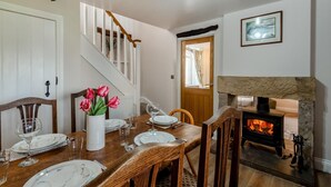 Et spiseområde med et træbord dækket til fire personer, en vase med røde blomster, en pejs og en trappe, der fører til et andet rum.