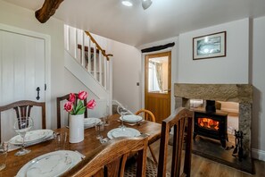 A dining area with a wooden table set for four, a vase with red flowers, a fireplace, and a staircase leading to another room. - 3 Bed in Papcastle (oc-c42478) (Papcastle)