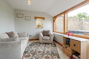 A cozy living room with a sofa, armchair, and a small table with a basket. There is a window with a stone wall outside. - 3 Bed in Papcastle (oc-c42478) (Papcastle)