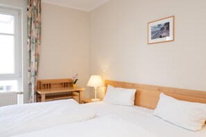 Una habitació d'hotel amb un llit, una tauleta de nit amb una làmpada, un escriptori petit, una cadira, una finestra amb cortines i un quadre encapçalat a la paret.