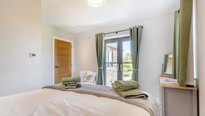 A bedroom with a bed, a wooden door, a window with curtains, and a view of the outside. - 5 Bed in Bluntisham (oc-m40249) (Bluntisham)