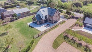 A modern two-story house with a large patio, surrounded by a well-maintained lawn and a gravel driveway. - 5 Bed in Bluntisham (oc-m40249) (Bluntisham)