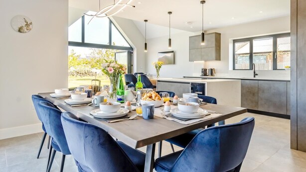 A modern dining area with a long table, blue chairs, and breakfast items. - 5 Bed in Bluntisham (oc-m40249) (Bluntisham)