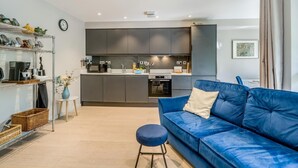 Et moderne køkken med lysegrå skabe, en blå sofa og et lille rundt bord.