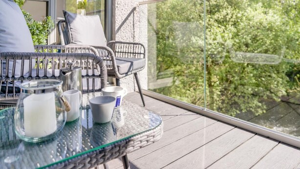 En balkon med fletmøbler, et glasbord og udsigt til grøn vegetation.